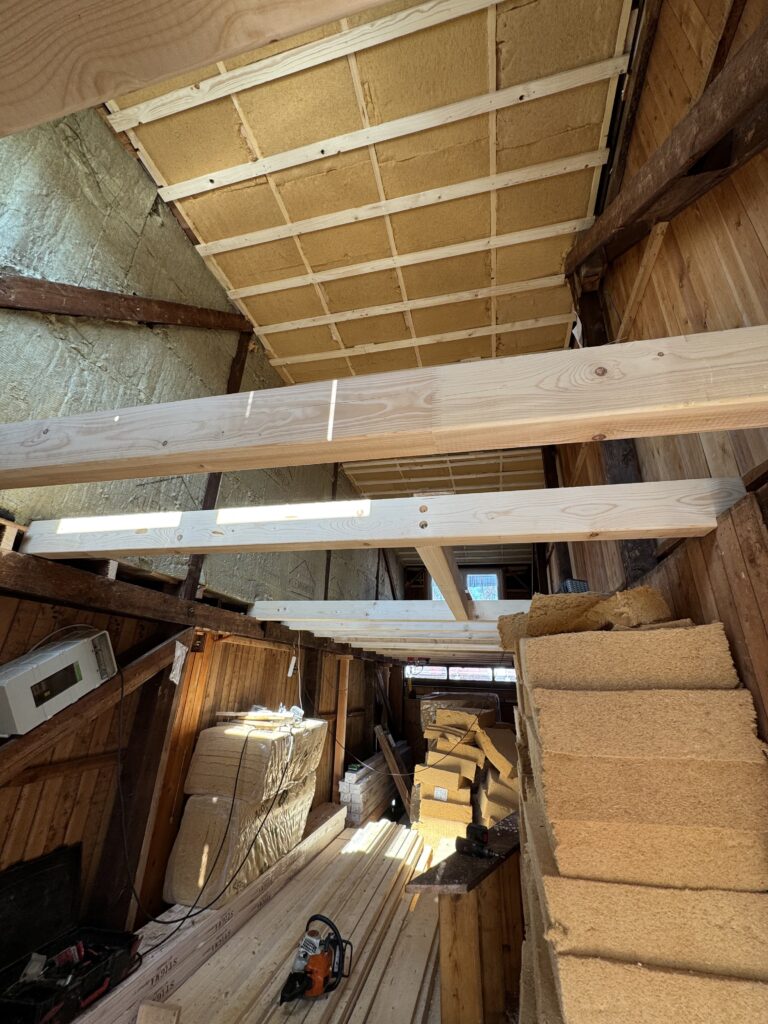 Blick aus dem Untergeschoss auf die Holzbalken, sowie die Dämmung im Dach aus Holzwolle